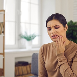 Woman in brown shirt with toothache needing an emergency dentist in Needham, MA