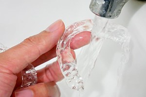 Hand holding Invisalign under running water in sink